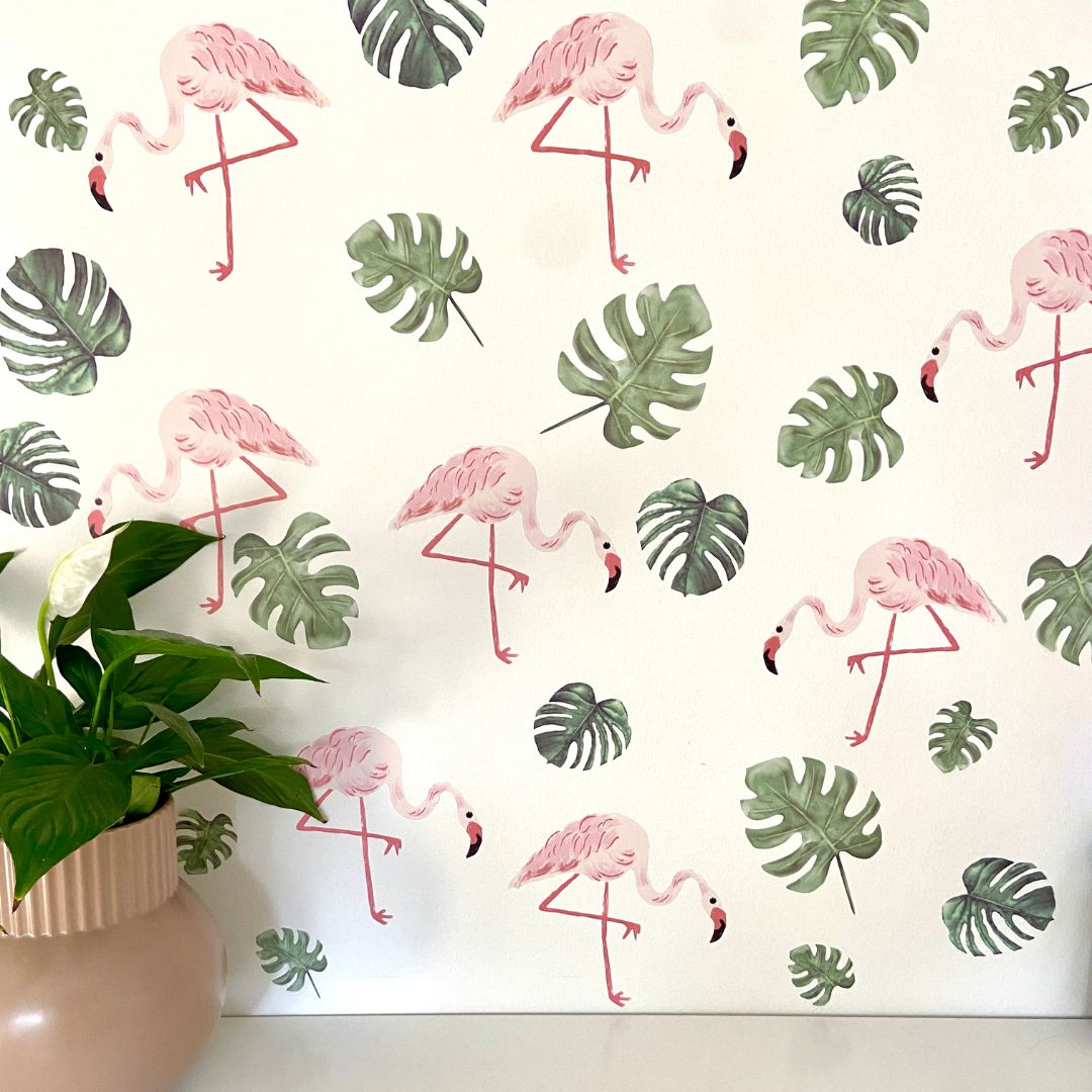 Bright pink flamingo wall decals surrounded by lush green leaves, designed for a playful and vibrant decor. The removable fabric decals are non-toxic, making them safe for any room.