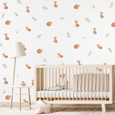 Adorable baby fox wall decals nestled among soft sage green leaves in a nursery. These non-toxic fabric decals are removable, ideal for creating a cozy and playful atmosphere in a child's room.