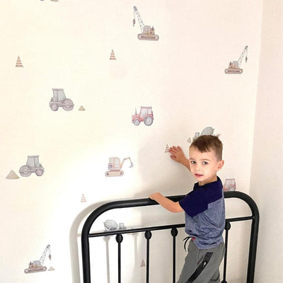 Picture of a bedroom with little boy applying  muted colourful diggers, trucks, excavators and pilon wall decals on the wall